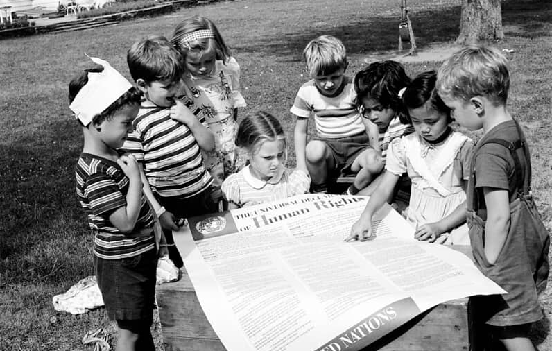 Grupo de niños/as alrededor de la declaración universal ® © UN Photo