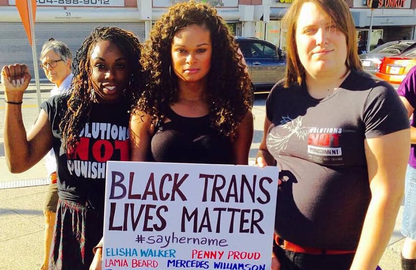 Tres mujeres protestan contra la transfobia y portan un cartel en el que se puede leer "Black Trans Lives Matter #SayHerName