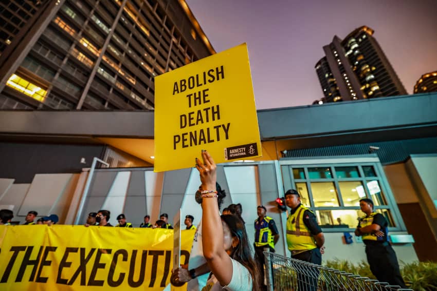 Activista sostiene cartel amarillo de Amnistía Internacional con el mensaje Abolish the death penalty durante una protesta contra la pena de muerte en Malasia y Singapur.
